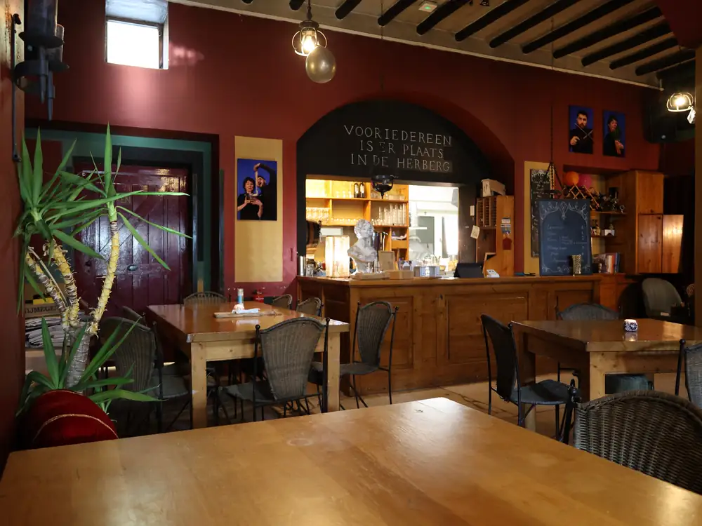Gezellige eetzaal met houten tafels, een bordeauxrode muur en de bar op de achtergrond